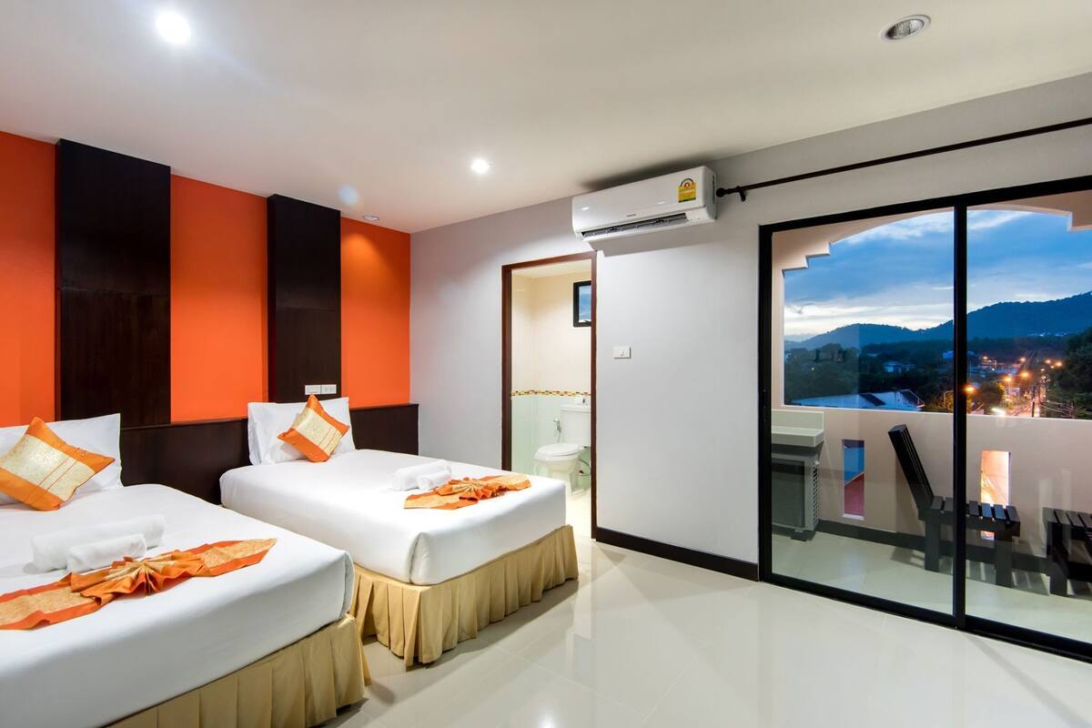 Una habitación de hotel moderna con dos camas, un equipo de aire acondicionado, un balcón con vistas a la ciudad y un ventanal grande.