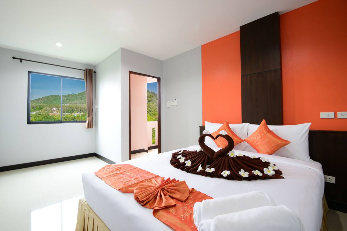 Una habitación de hotel con una cama grande, vistas a un paisaje verde y una pared anaranjada de estilo moderno.