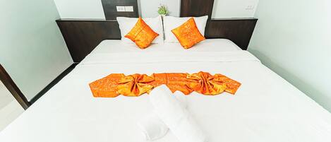 A neatly made bed with white linens and orange decorative pillows, a rolled white towel, and an orange ribbon.