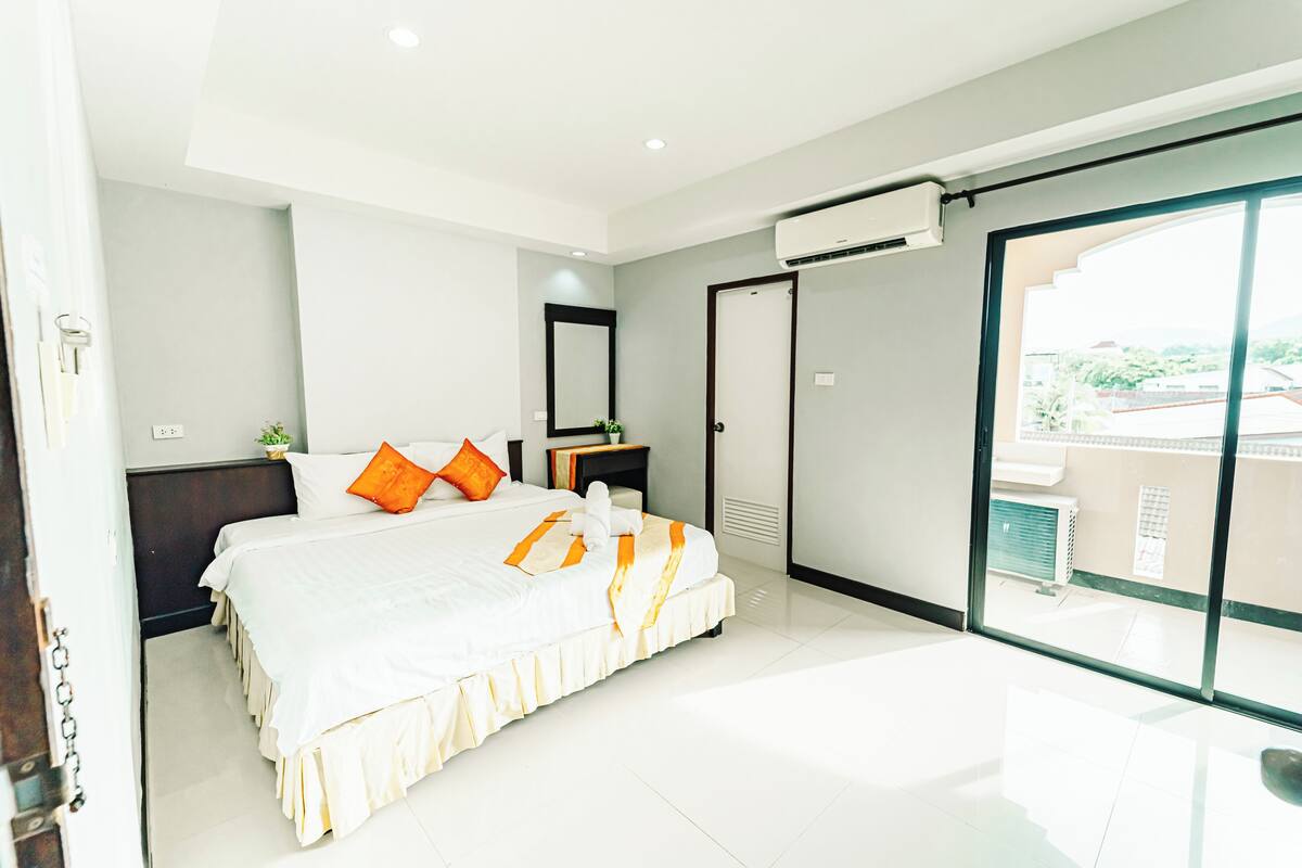 Una habitación de hotel moderna con una cama grande, una mesita de noche, un espejo y un ventanal corredero que da a un balcón.