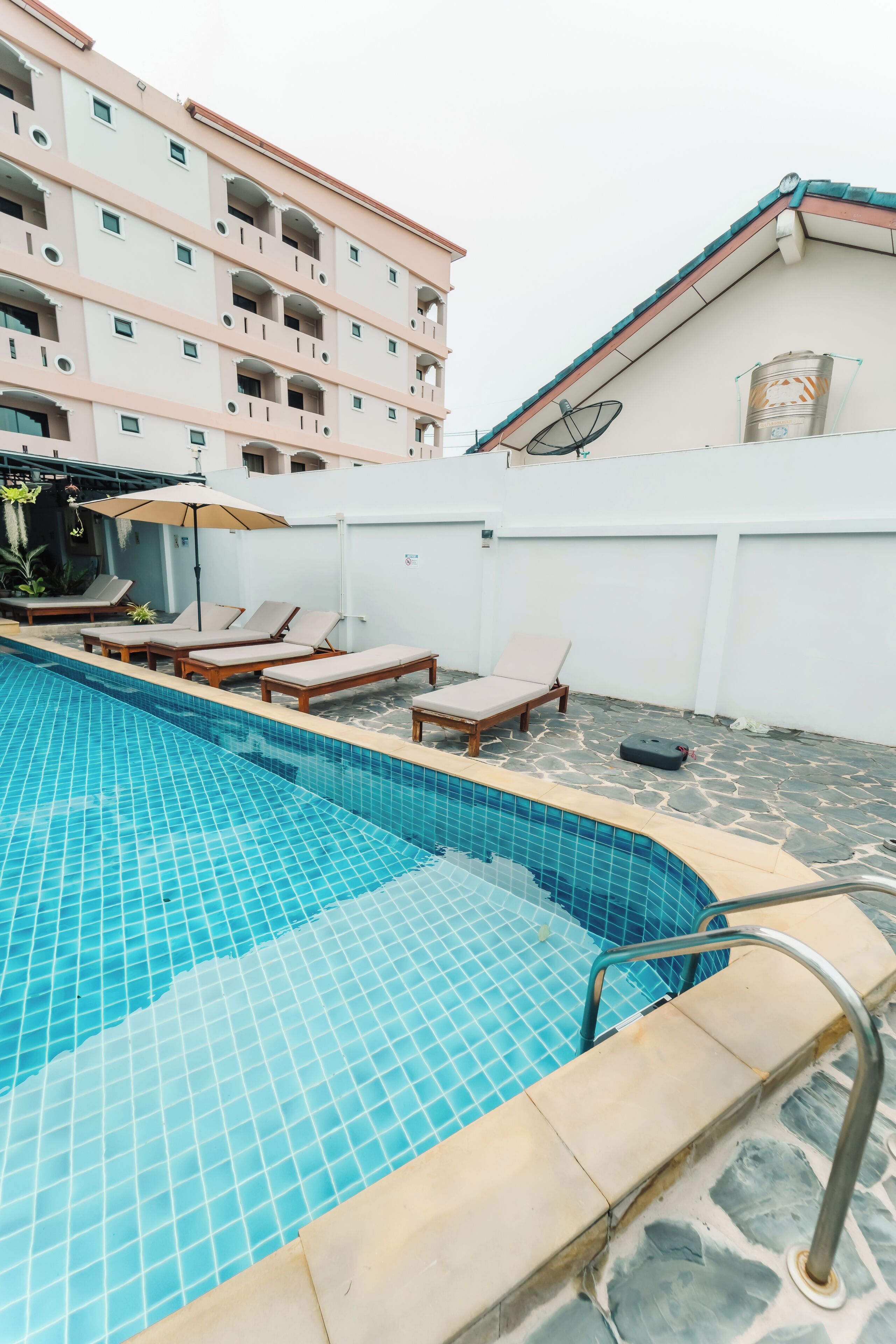 A swimming pool with tiled edges, lounge chairs, and a building with balconies in the background.