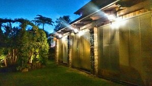 Un edificio con un espacio exterior cubierto, pilares de piedra y una valla de metal.