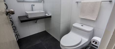 A modern bathroom with a white sink, black floor tiles, a toilet, and a towel hanging on the wall.