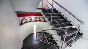 A spiral staircase with metal railings and black steps, leading to a landing with a red accent wall and decorative vases. - Hotel El Sol (Piura)