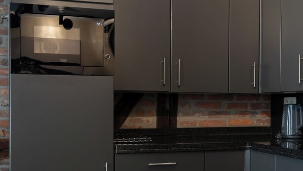 A modern kitchen with dark cabinetry, a built-in oven, and a coffee maker. - Amosa Liège City Centre Apart Gerardrie 23 (Liege)