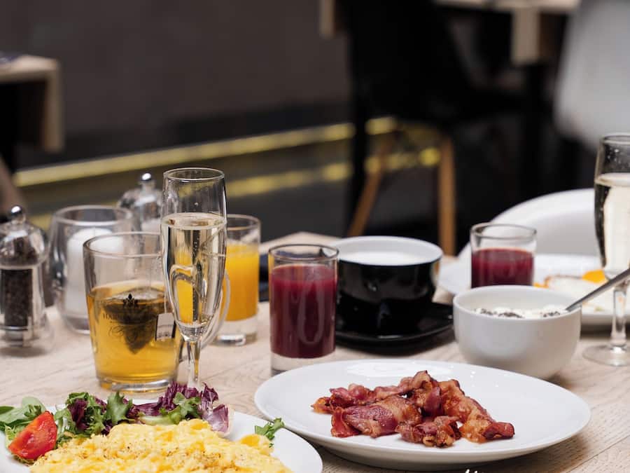 A breakfast setting with plates of scrambled eggs, bacon, and a salad, along with various beverages and a glass of champagne.
