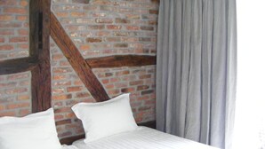 Una cama con ropa blanca en una habitación con paredes de ladrillo visto y vigas de madera.