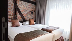 A hotel room with two beds, a brick wall, and a large window with curtains. - Amosa Liège City Centre Apart Gerardrie 23 (Liege)