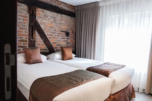 Habitación de hotel con dos camas, una pared de ladrillo y un ventanal con cortinas.