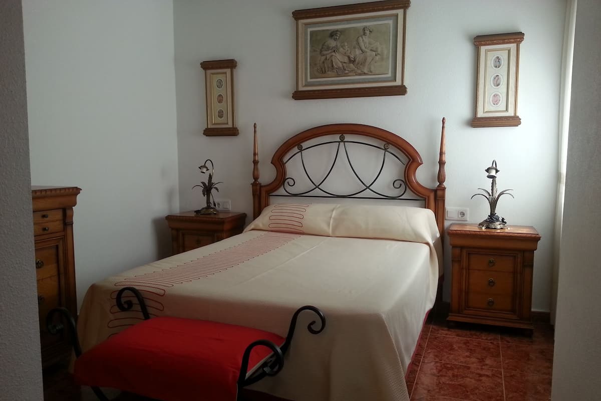 Un lit bien fait, agrémenté d’un couvre-lit rouge, d’une tête de lit en bois et de deux tables de chevet avec des lampes.