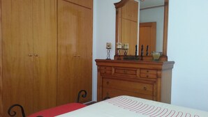 Un dormitorio con un armario de madera, un tocador con espejo y una cama con colcha roja.