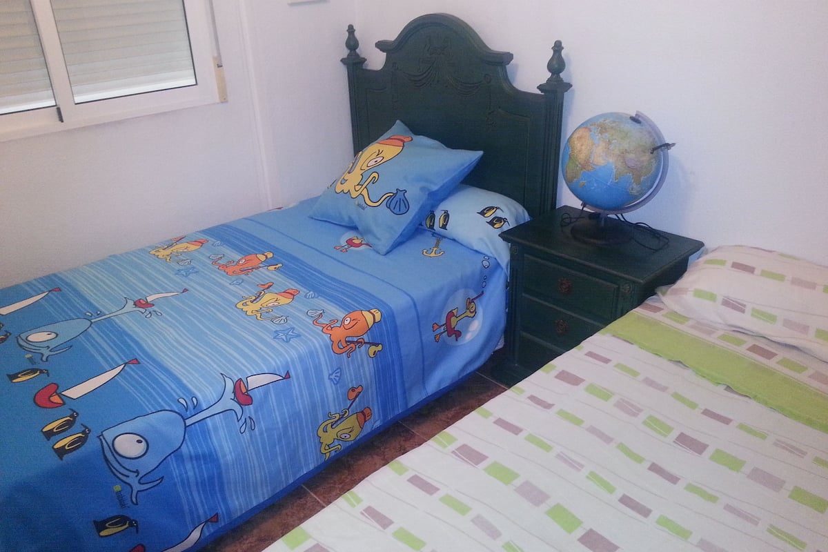 Une chambre avec un lit sur le côté gauche, une commode sur laquelle repose un globe terrestre, et une fenêtre avec des stores.