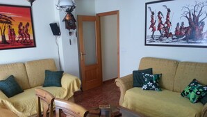 Una sala de estar con dos sofás, una silla de madera, una mesa de centro de vidrio y una puerta.