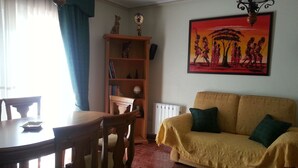 Una sala de estar con una mesa de comedor, sillas, un sofá, una estantería y un cuadro en la pared.