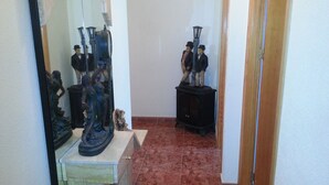 Un pasillo con suelo de baldosas, un espejo que refleja estatuas y una puerta a la derecha.