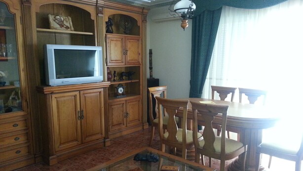 Una sala de estar con un aparador de madera, una mesa de centro de vidrio y un comedor con sillas y mesa de madera.