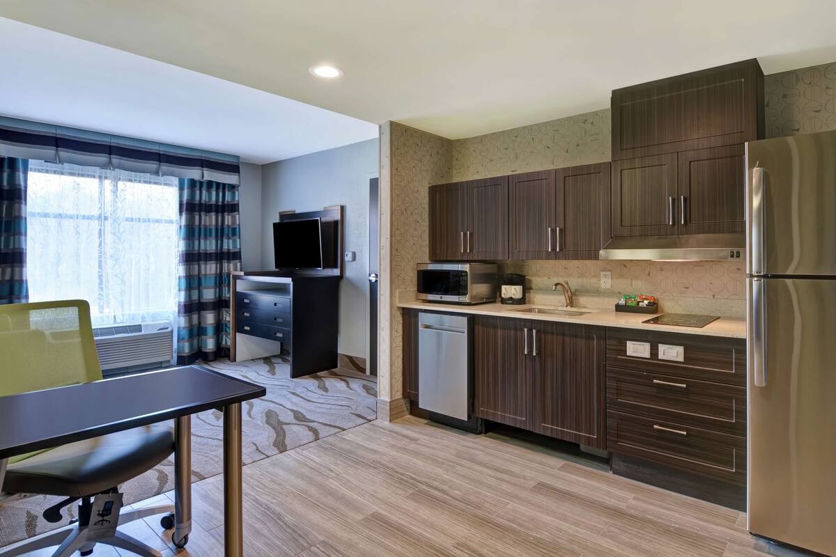 A modern kitchen with dark wood cabinets, stainless steel appliances, and a large window with curtains.
