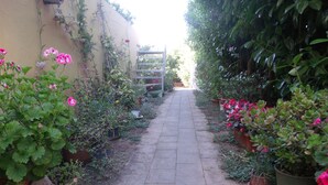 Um caminho de pedra estreito, ladeado por vasos de plantas e flores, que leva a um portão.