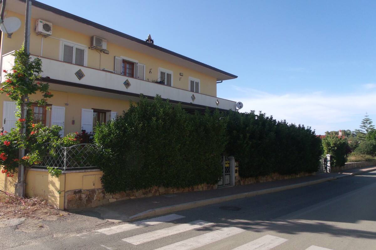 Un edificio de dos pisos con fachada amarilla, contraventanas blancas y múltiples unidades de aire acondicionado.