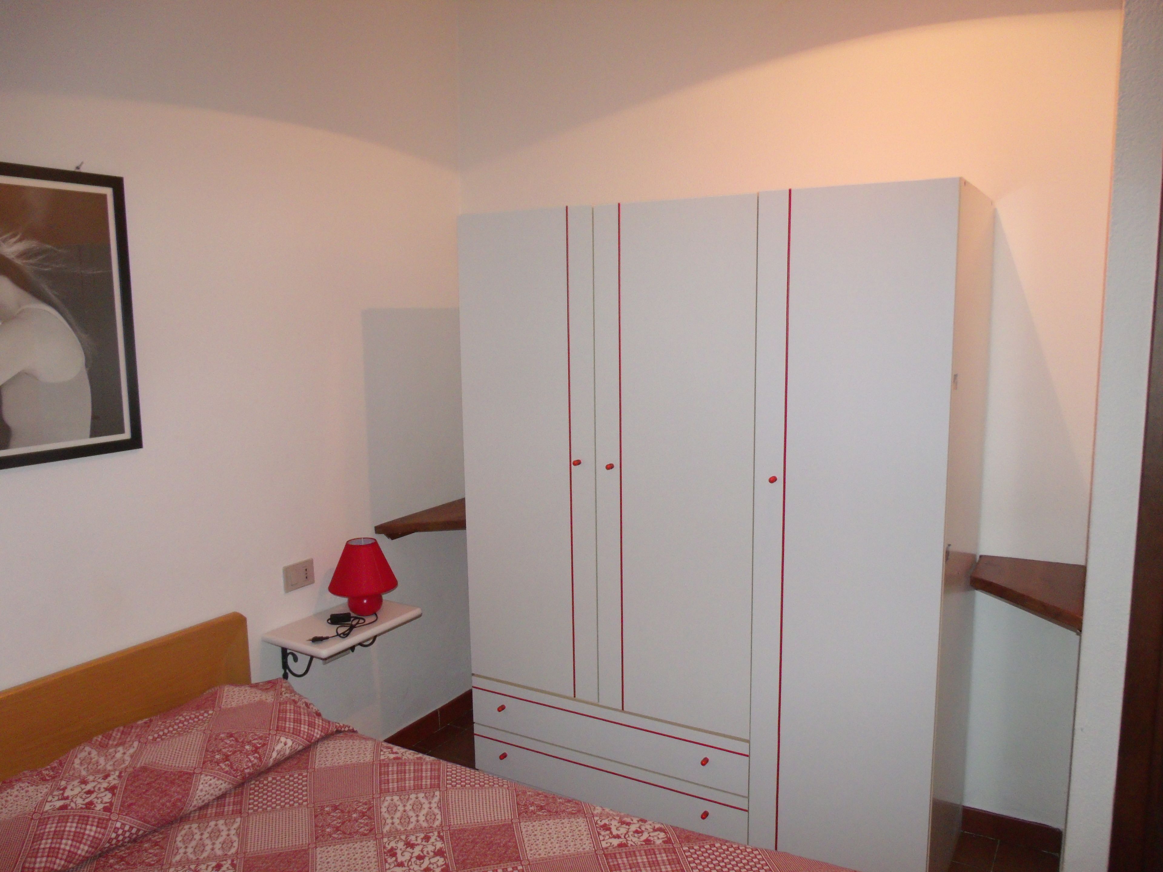 A bedroom with a bed, a wardrobe, a bedside table, and a lamp.