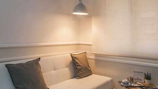 Ein stilvolles Wohnzimmer mit einem weißen Sofa, einem kleinen Tisch mit Teekanne und einer Deckenleuchte.