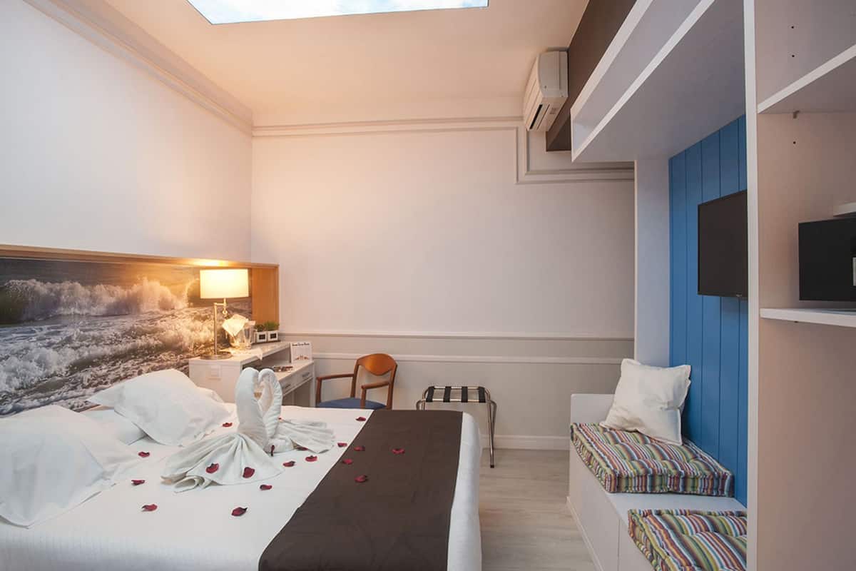 Quarto de hotel com cama, escrivaninha, poltrona, televisão e vista para o oceano.