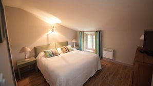 A bedroom with a large bed, two bedside lamps, a window with curtains, and a television on a wooden cabinet. - Chateau Cicéron (Ribaute)