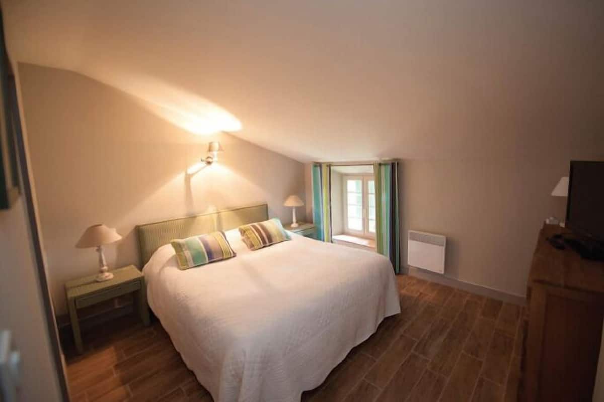 A bedroom with a large bed, two bedside lamps, a window with curtains, and a television on a wooden cabinet.