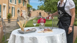 A woman pouring wine into a glass at an outdoor table with bread and flowers. - Chateau Cicéron (Ribaute)