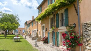A row of traditional Mediterranean-style buildings with stone steps leading to the entrance, a well-maintained lawn, and outdoor seating area. - Chateau Cicéron (Ribaute)