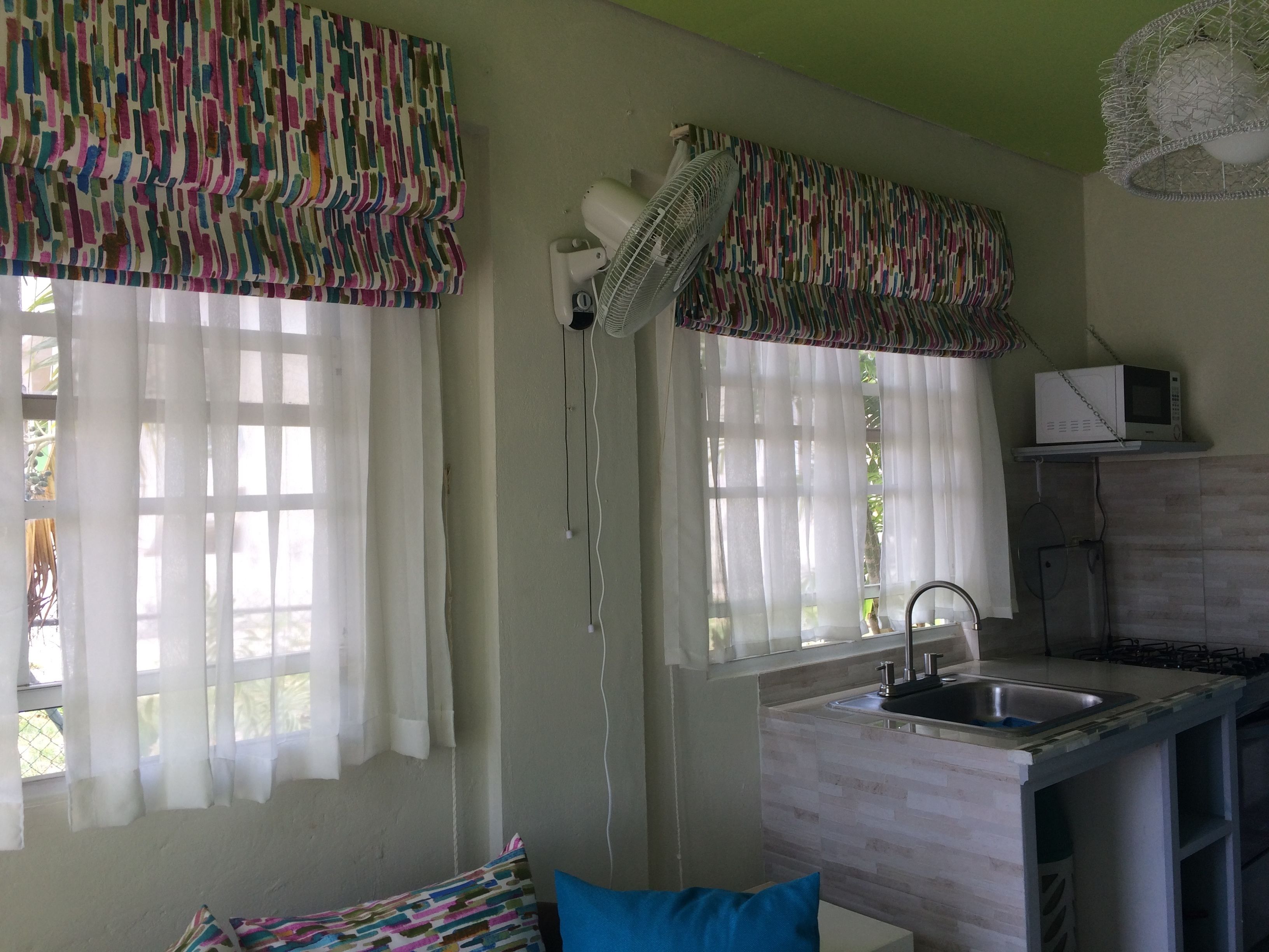 Uma cozinha compacta com pia, micro-ondas e ventilador.