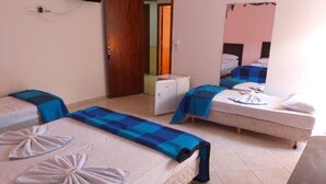 Habitación de hotel con dos camas, cada una con colcha y toallas de cuadros azules y blancos dispuestas en forma de abanico. Hay un refrigerador blanco pequeño y un espejo en la pared.