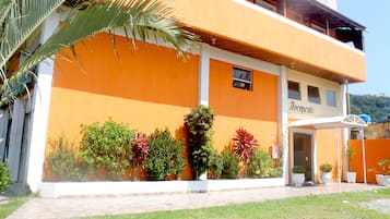 Um edifício de dois andares com uma área de recepção, rodeado por diversas plantas em vasos e uma palmeira.