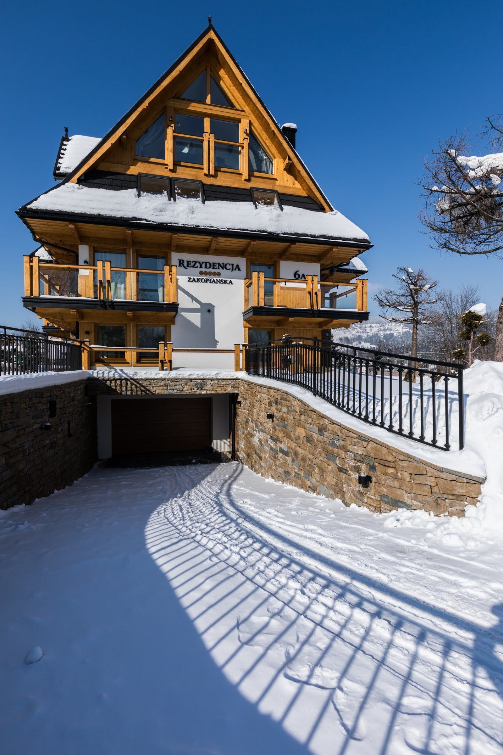 A wooden chalet with a balcony, a stone entrance, and a sign indicating it is a ski resort.