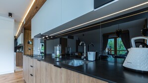A modern kitchen with a black countertop, stainless steel sink, and wooden cabinets. - Rezydencja Zakopiańska (Zakopane)