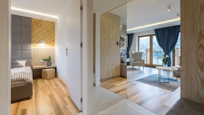 A modern hotel room with a wooden floor, a bed with a headboard, a bedside table with a lamp, and a large mirror reflecting the room. - Rezydencja Zakopiańska (Zakopane)