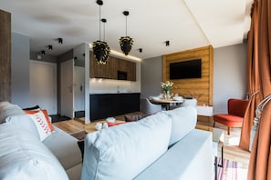 Uma sala de estar moderna com sofá, mesa de jantar e cozinha com armários de madeira e uma televisão de tela plana.