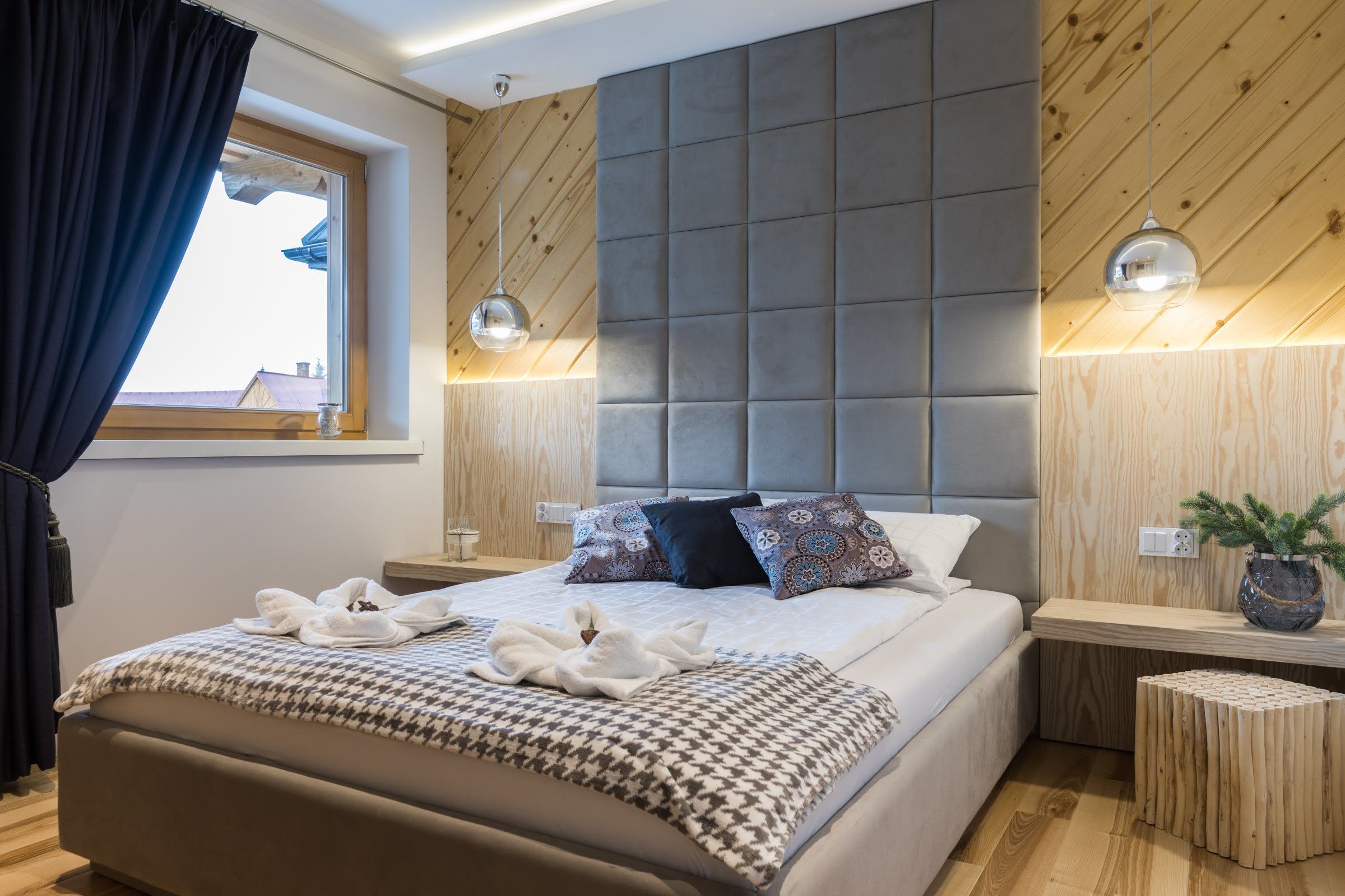 A modern hotel room with a large bed, a wooden headboard, and a window with curtains.