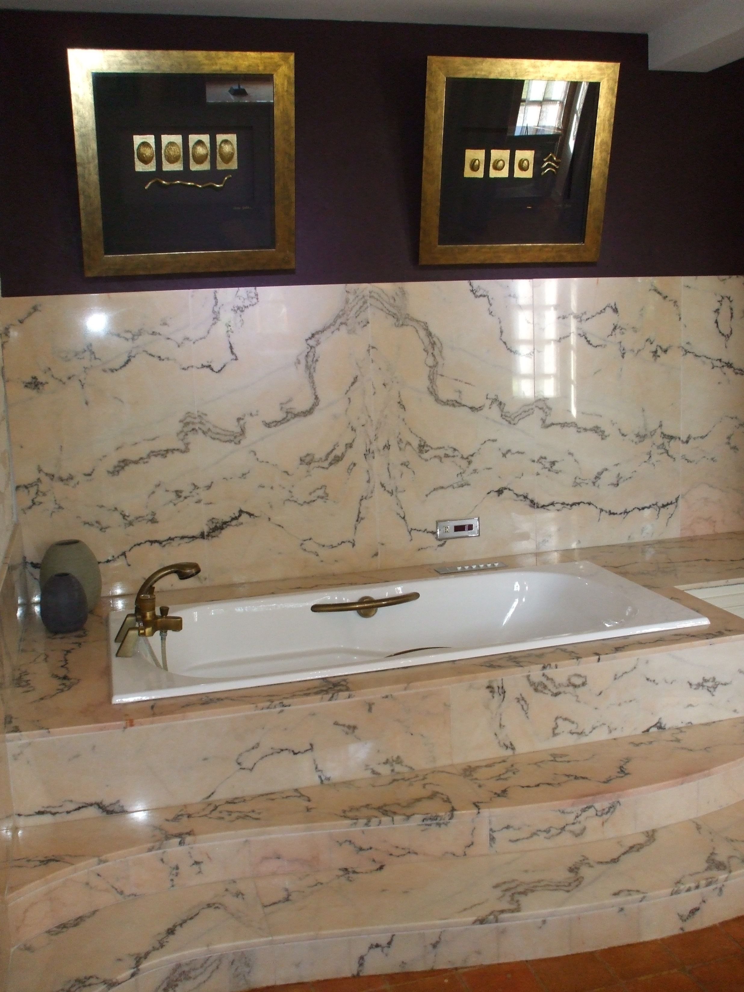 Un baño con un lavamanos de mármol, una bañera y dos espejos enmarcados en la pared.