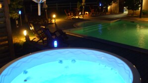 A hot tub with a wavy edge design, surrounded by lounge chairs and umbrellas, with a pool in the background. - Chambres d'hôtes au clos de Beaulieu (Bossée)