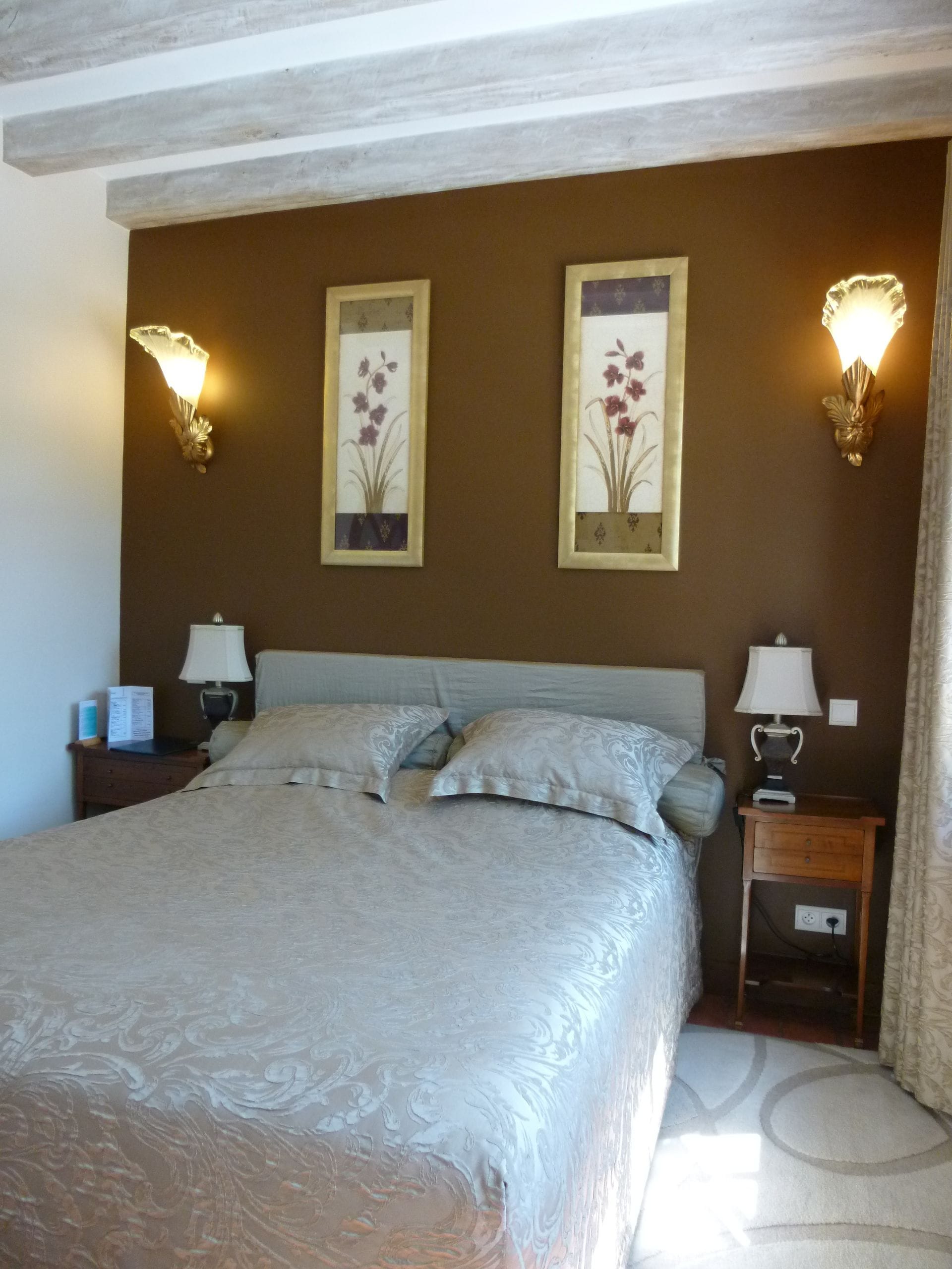 A bedroom with a large bed, two wall-mounted lamps, and two framed floral artworks.