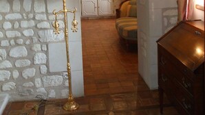 A stone-walled room with a wooden dresser, a lamp, and a view into a kitchen area with cabinets and a dining table. - Chambres d'hôtes au clos de Beaulieu (Bossée)