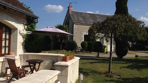 A patio area with outdoor furniture, a stone wall, and a view of a building with a tiled roof. - Chambres d'hôtes au clos de Beaulieu (Bossée)