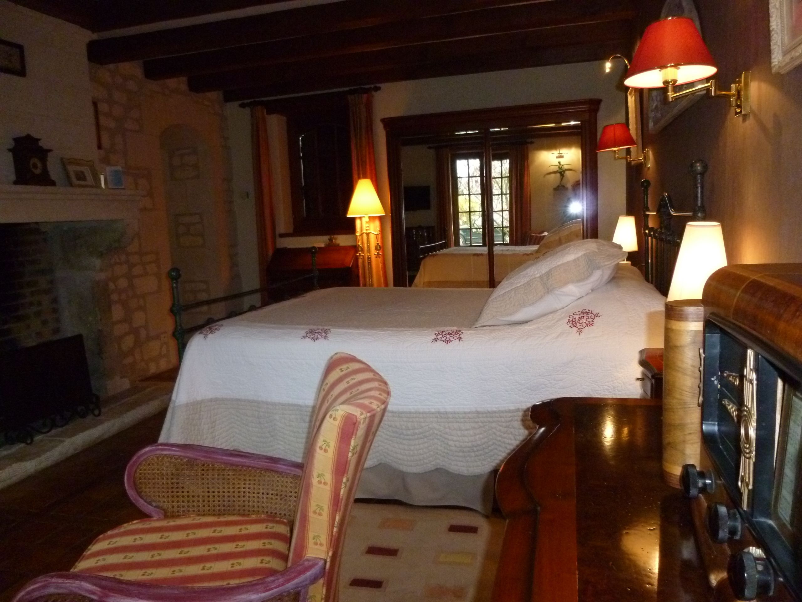A bedroom with a bed, a chair, a fireplace, and wall-mounted lamps.