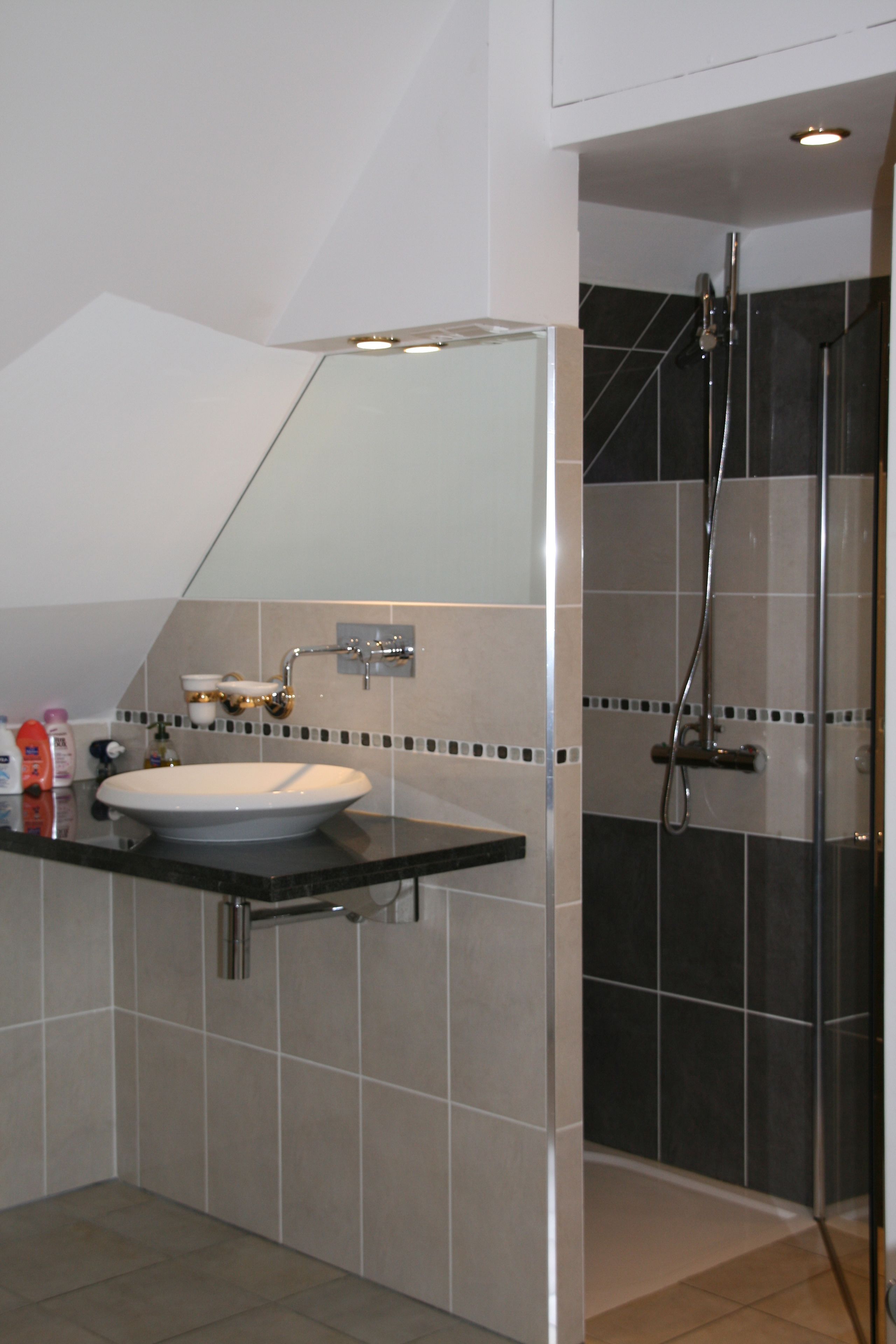 Un baño con lavamanos blanco, baldosas oscuras y zona de ducha.