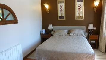 A bedroom with a large bed, two bedside tables with lamps, a window with a wooden frame, and two wall-mounted light fixtures.