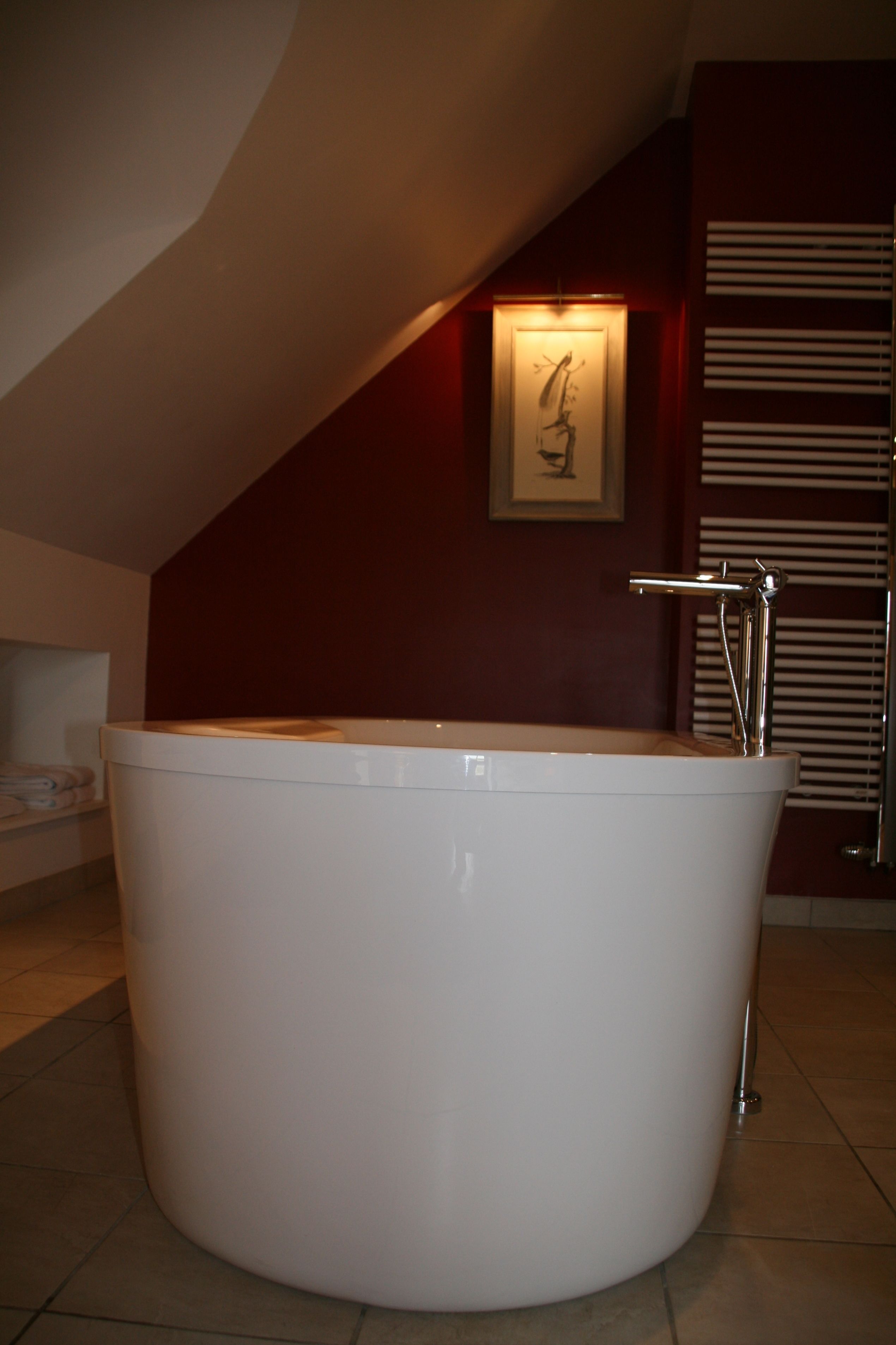 A large, white bathtub in a room with a sloped ceiling and a framed picture on the wall.