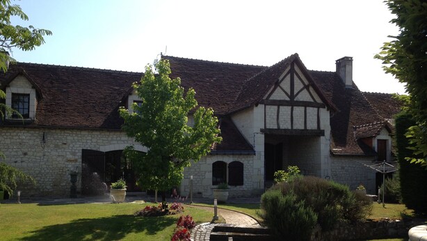 A stone building with a tiled roof, a paved pathway, and a small garden area with a tree and shrubs. - Chambres d'hôtes au clos de Beaulieu (Bossée)