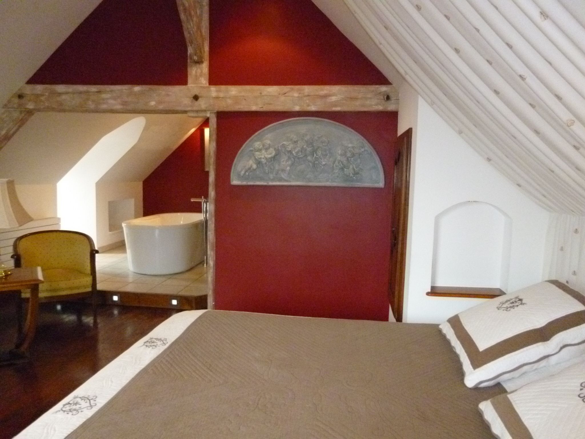 Un dormitorio con cama, una silla, una bañera y una obra de arte en la pared.