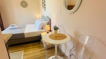A compact hotel room with a bed, a small table with a lamp, a mirror, and two chairs.